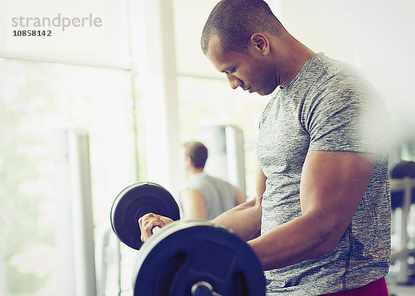 Fokussierter Mann  der Barbell-Bizeps-Locken in der Turnhalle macht.