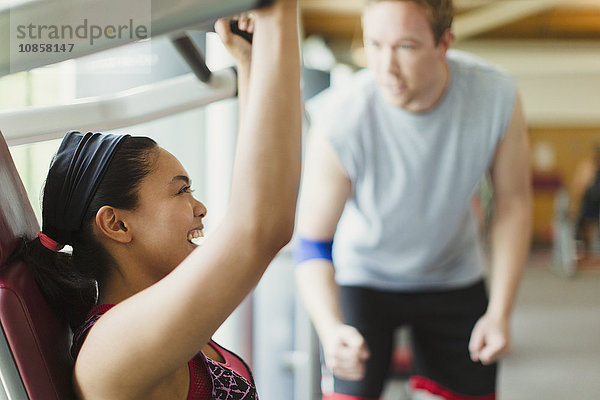 Personal Trainerin  die eine begeisterte Frau mit Trainingsgeräten im Fitnessstudio führt.