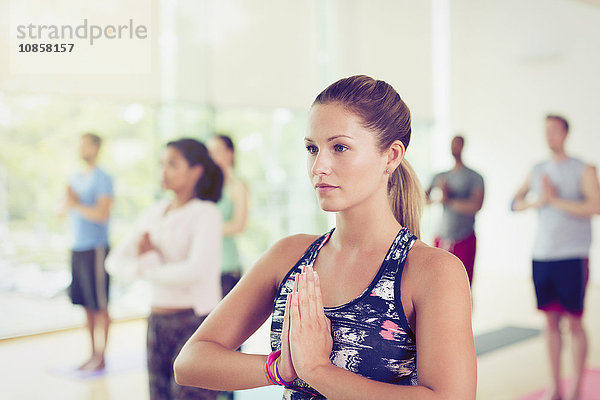 Fokussierte Frau mit Händen in Gebetsposition in der Yogastunde