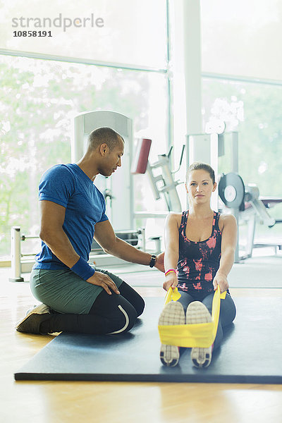 Personal Trainerin führt Frau beim Stretchen der Beine mit Widerstandsband im Fitnessstudio