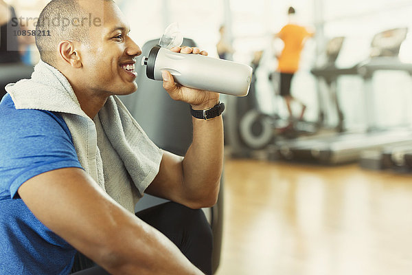 Lächelnder Mann trinkt Wasser im Fitnessstudio