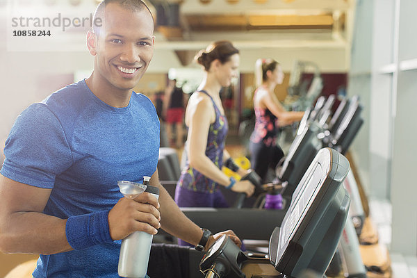 Portrait lächelnder Mann mit Wasserflasche auf dem Laufband im Fitnessstudio