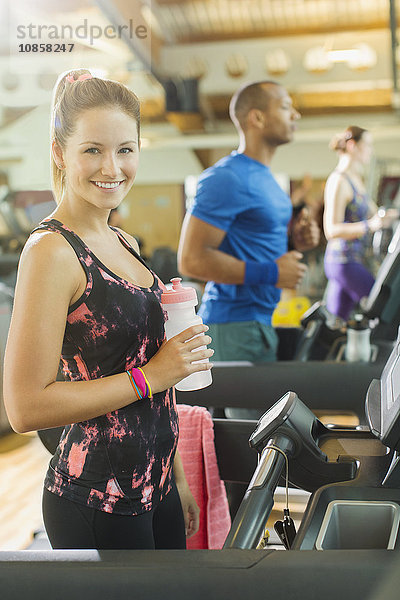 Portrait lächelnde Frau mit Wasserflasche auf dem Laufband im Fitnessstudio