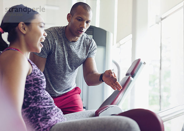 Personal Trainerin  die die Frau auf dem Trainingsgerät im Fitnessstudio führt.