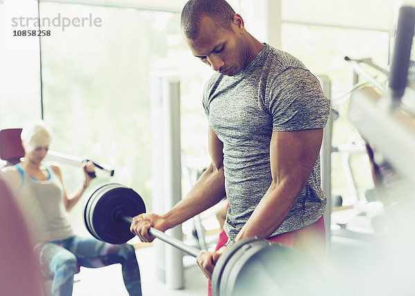 Fokussierter Mann  der Barbell-Bizeps-Locken in der Turnhalle macht.