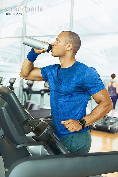 Mann Trinkwasser auf dem Laufband im Fitnessstudio