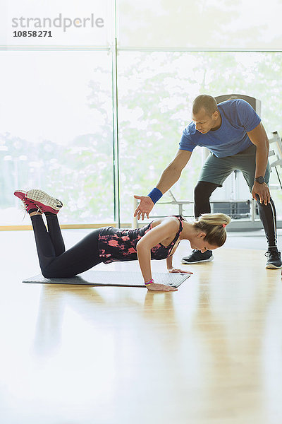 Personal Trainerin  die die Frau beim Push-Up auf den Knien im Fitnessstudio führt.