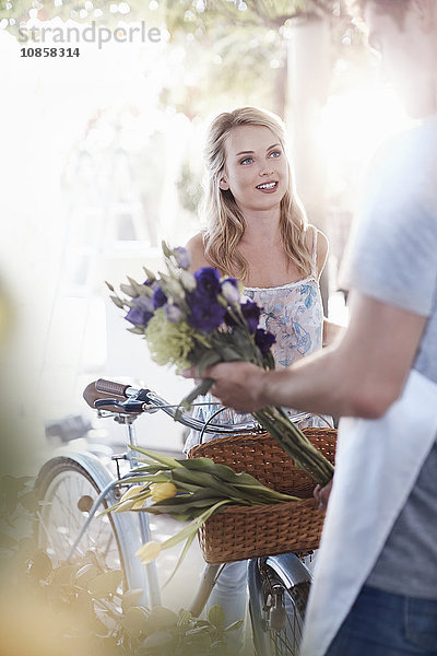 Florist legt Blumen in den Korb auf dem Fahrrad der Frau