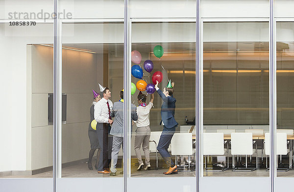 Verspielte Geschäftsleute in Partyhüten feiern mit Luftballons im Konferenzraum