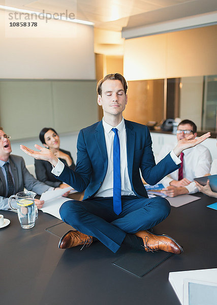 Kollegen beobachten zen-ähnliche Geschäftsleute  die in Lotusstellung auf dem Konferenztisch meditieren.