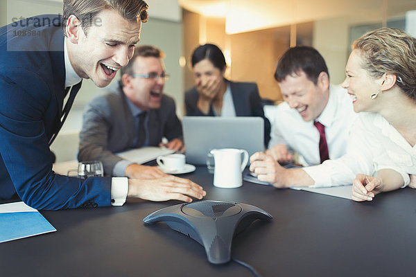 Lachende Geschäftsleute bei einer Telefonkonferenz im Konferenzraum