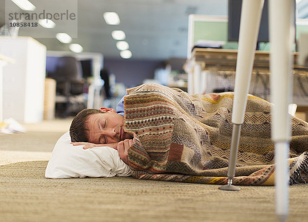 Geschäftsmann mit Kissen und Decke schlafend im Bürogeschoss