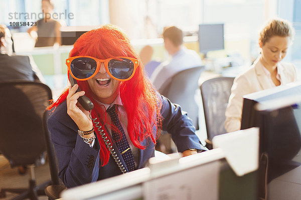 Portrait Verspielter Geschäftsmann mit roter Perücke und großer Sonnenbrille im Büro