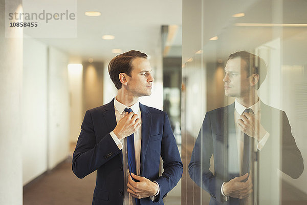 Zuversichtlicher Geschäftsmann beim Anpassen der Krawatte im Büroflur