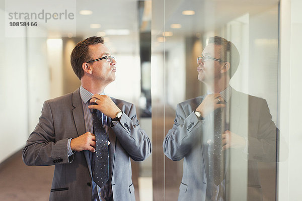 Spiegelung des selbstbewussten Geschäftsmannes bei der Anpassung der Krawatte im Büroflur