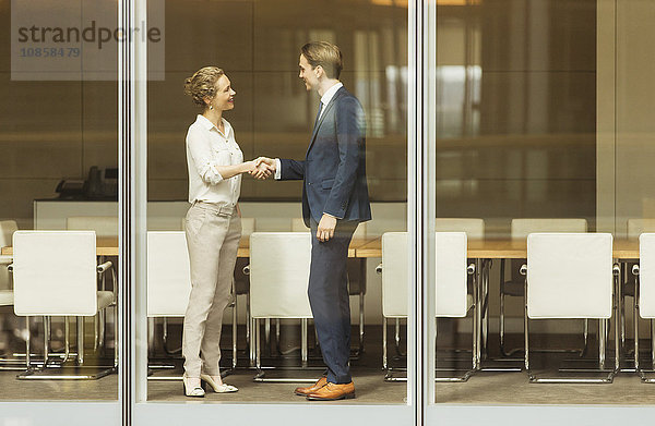 Geschäftsmann und Geschäftsfrau beim Händeschütteln am Konferenzraumfenster