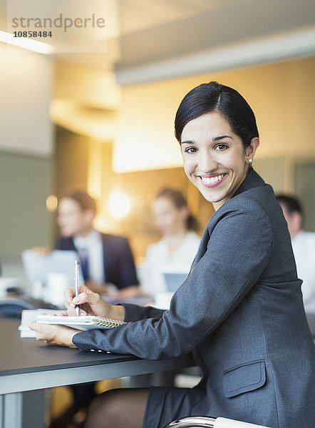 Porträt einer lächelnden Geschäftsfrau  die sich Notizen im Konferenzraum macht.