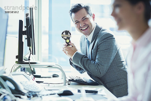 Porträt eines begeisterten Geschäftsmannes mit Siegerpokal am Schreibtisch im Büro