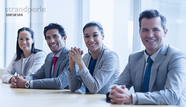 Portrait von lächelnden Geschäftsleuten  die in einer Reihe im Konferenzraum sitzen.