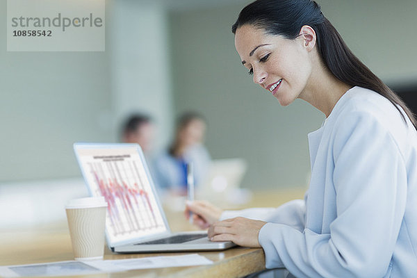 Lächelnde Geschäftsfrau bei der Arbeit am Laptop mit Kaffee im Konferenzraum