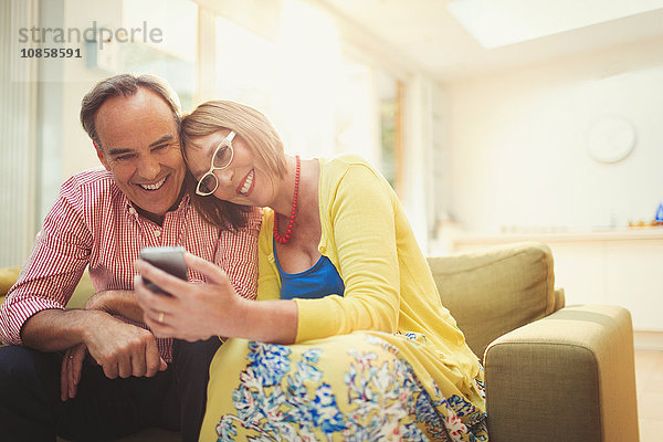 Lächelndes reifes Paar SMS mit Handy im Wohnzimmer