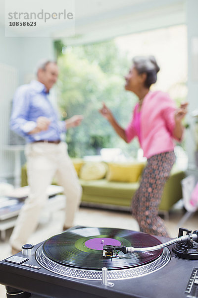 Verspieltes Naturpaar tanzt im Wohnzimmer hinter dem Plattenspieler