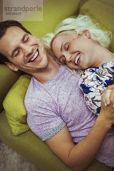 Liebevoll lachendes Paar auf dem Sofa liegend mit geschlossenen Augen