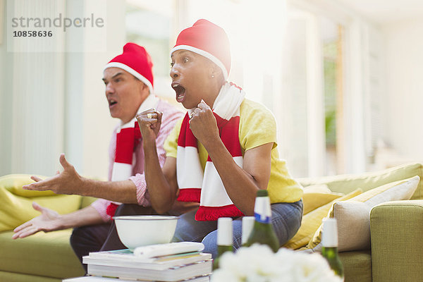 Jubelndes reifes Paar mit passenden Hüten und TV-Sportereignis im Wohnzimmer