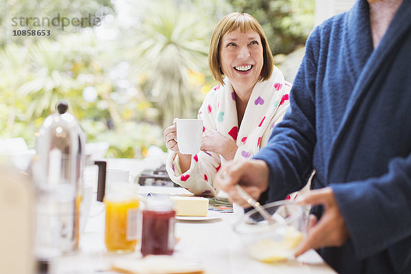 Lächelnde reife Frau beim Kaffeetrinken im Bademantel zum Frühstück