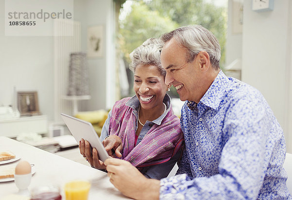 Lächelndes reifes Paar  das sich ein digitales Tablett am Frühstückstisch teilt.
