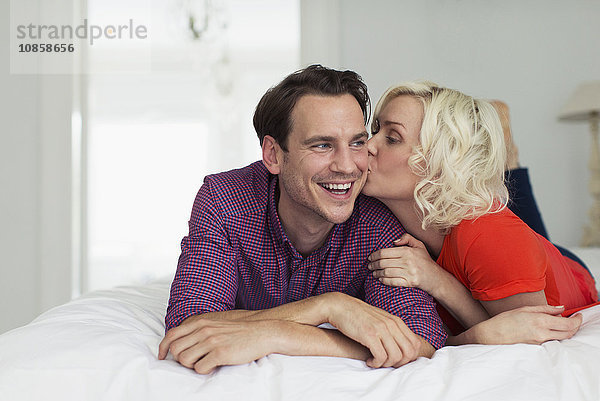 Zärtliche Frau küsst lächelnden Ehemann auf dem Bett
