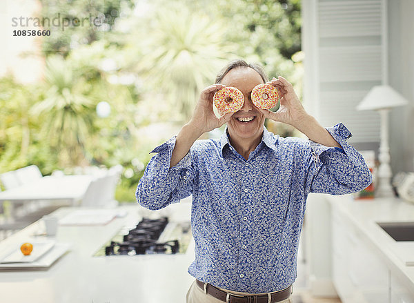 Portrait Verspielter reifer Mann  der die Augen mit Donuts bedeckt.