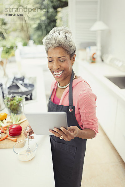 Lächelnde reife Frau mit digitalem Tablettenkochen in der Küche