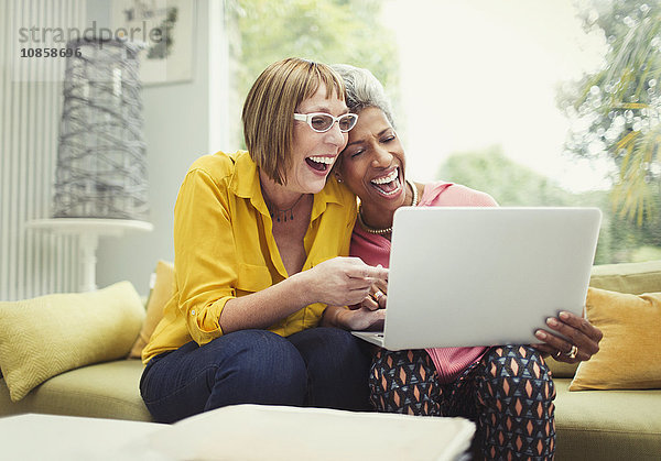 Lachende reife Frauen teilen Laptop auf Wohnzimmer-Sofa