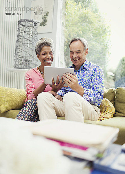 Lächelndes reifes Paar teilt sich ein digitales Tablett auf dem Wohnzimmersofa