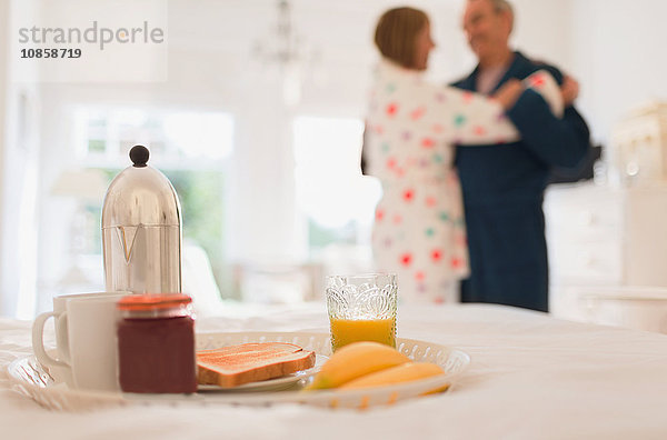 Reife Paare im Bademantel tanzen hinter dem Frühstück im Bett