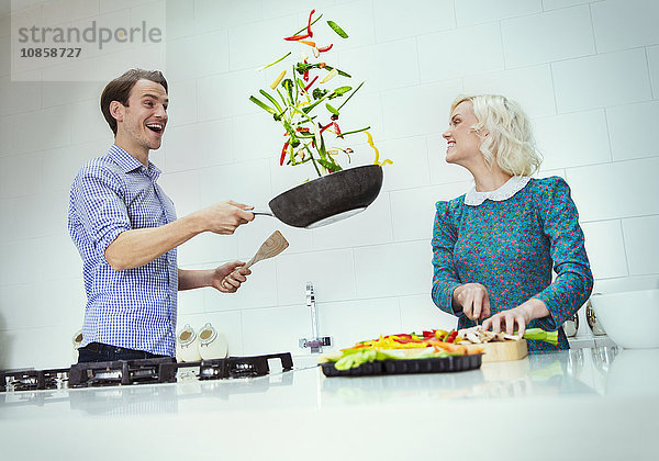 Überraschtes Paar beim Kochen von Gemüse in der Pfanne in der Küche