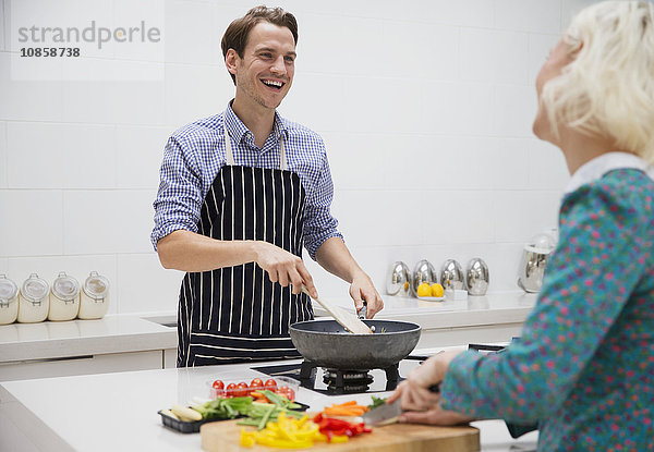 Lächelndes Paar beim Schneiden und Kochen von Gemüse in der Küche