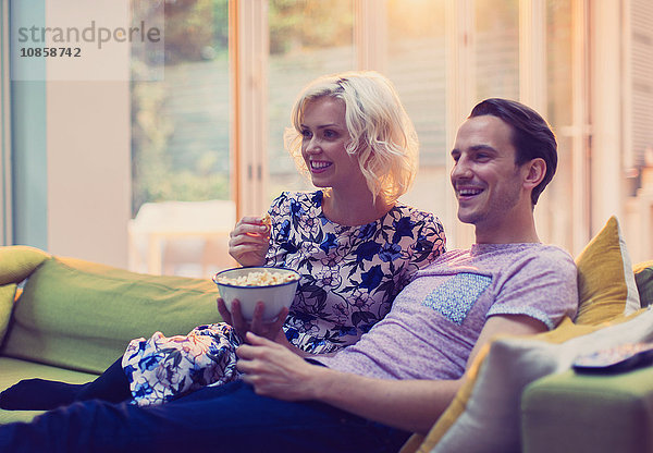 Paar sieht fern und isst Popcorn auf dem Wohnzimmersofa.