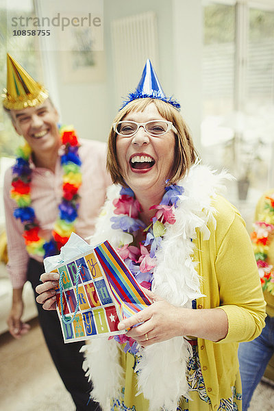 Portrait lachende reife Frau im Partyhut mit Geburtstagsgeschenk