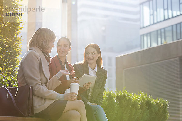 Lächelnde Geschäftsfrauen mit digitalem Tablett beim Kaffee trinken im Freien