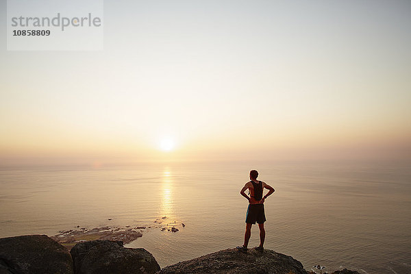 Männlicher Läufer auf Felsen mit Blick auf den Sonnenuntergang und Meerblick