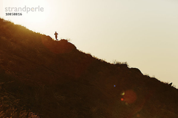 Silhouette des Läufers  der bei Sonnenuntergang den Hang hinaufsteigt