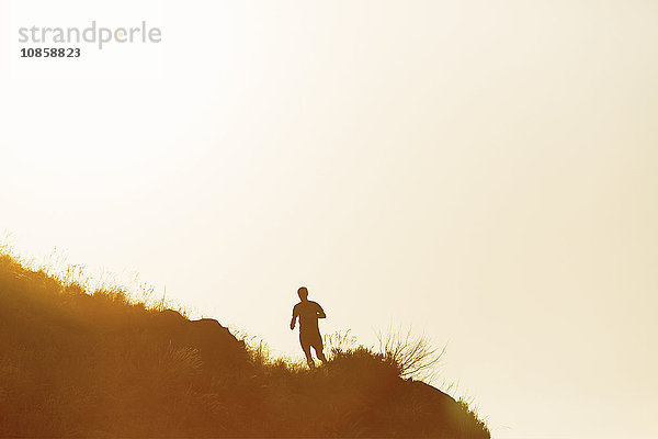 Silhouette eines Mannes  der bei Sonnenuntergang auf dem Hügel läuft.