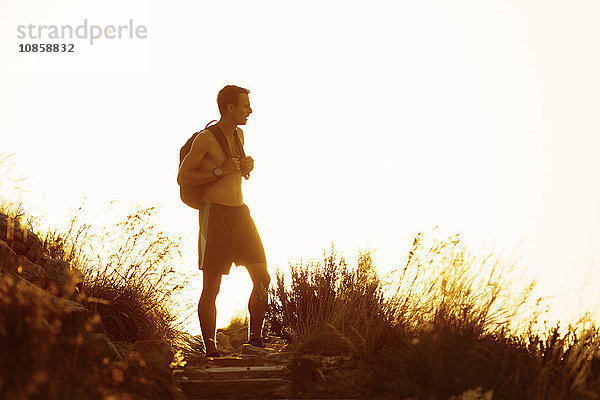 Nackter männlicher Wanderer mit Rucksack bei Sonnenuntergang auf dem Weg