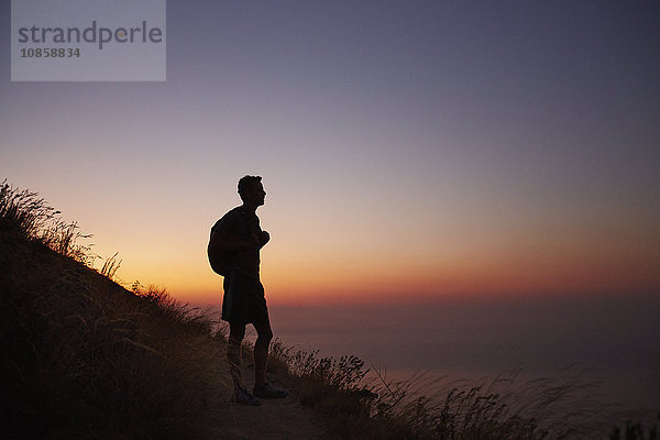 Silhouette des männlichen Wanderers auf dem Weg zum Meer bei Sonnenuntergang
