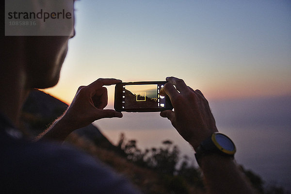 Mann fotografiert Sonnenuntergang mit Fotohandy