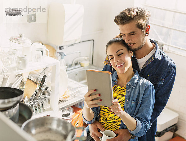 Liebevolles junges Paar mit digitalem Tablett in der Wohnküche
