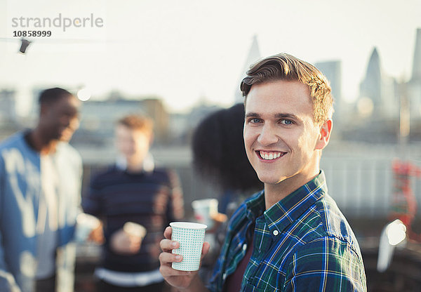 Portrait lächelnder junger Mann beim Trinken auf der Dachparty