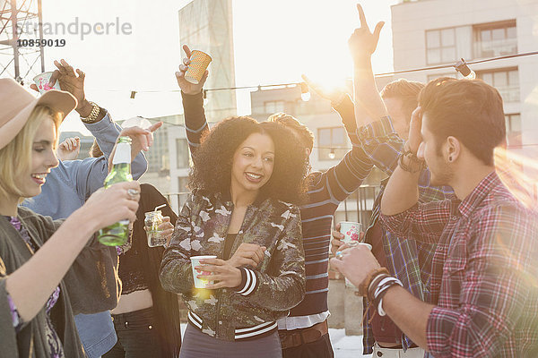 Begeisterte junge erwachsene Freunde beim Tanzen und Trinken auf der Dachparty